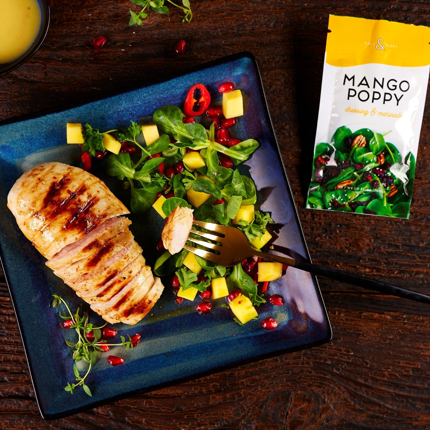Mango Poppy single serve salad dressing packet next to plate with mango salad and chicken.
